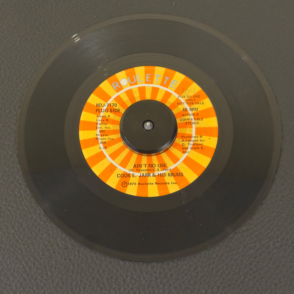 7" vinyl record by Cook E. Jarr & His Crumbs featuring "Ain't No Use/(Part 2) (Instrumental)", released on Roulette (RDJ-7170), in NM (Near Mint) condition, classic analog collectable for turntable playback. Promo copy with original sleeve!  Before cementing his status as an iconic, Vegas entertainment legend, Cook E. Jarr cut some of the nastiest East Coast funk-crossover of the mid-70s. WOL
