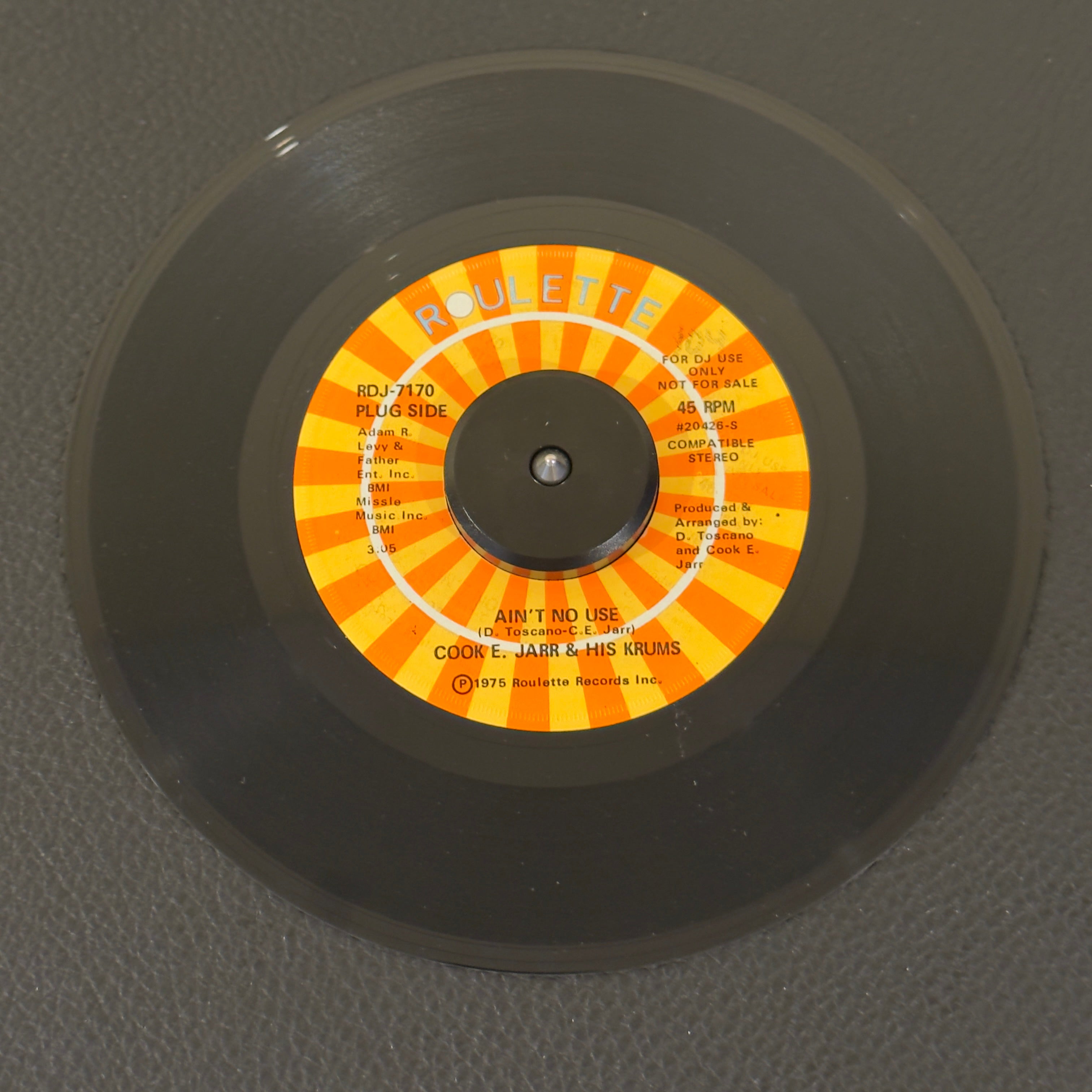 7" vinyl record by Cook E. Jarr & His Crumbs featuring "Ain't No Use/(Part 2) (Instrumental)", released on Roulette (RDJ-7170), in NM (Near Mint) condition, classic analog collectable for turntable playback. Promo copy with original sleeve!  Before cementing his status as an iconic, Vegas entertainment legend, Cook E. Jarr cut some of the nastiest East Coast funk-crossover of the mid-70s. WOL