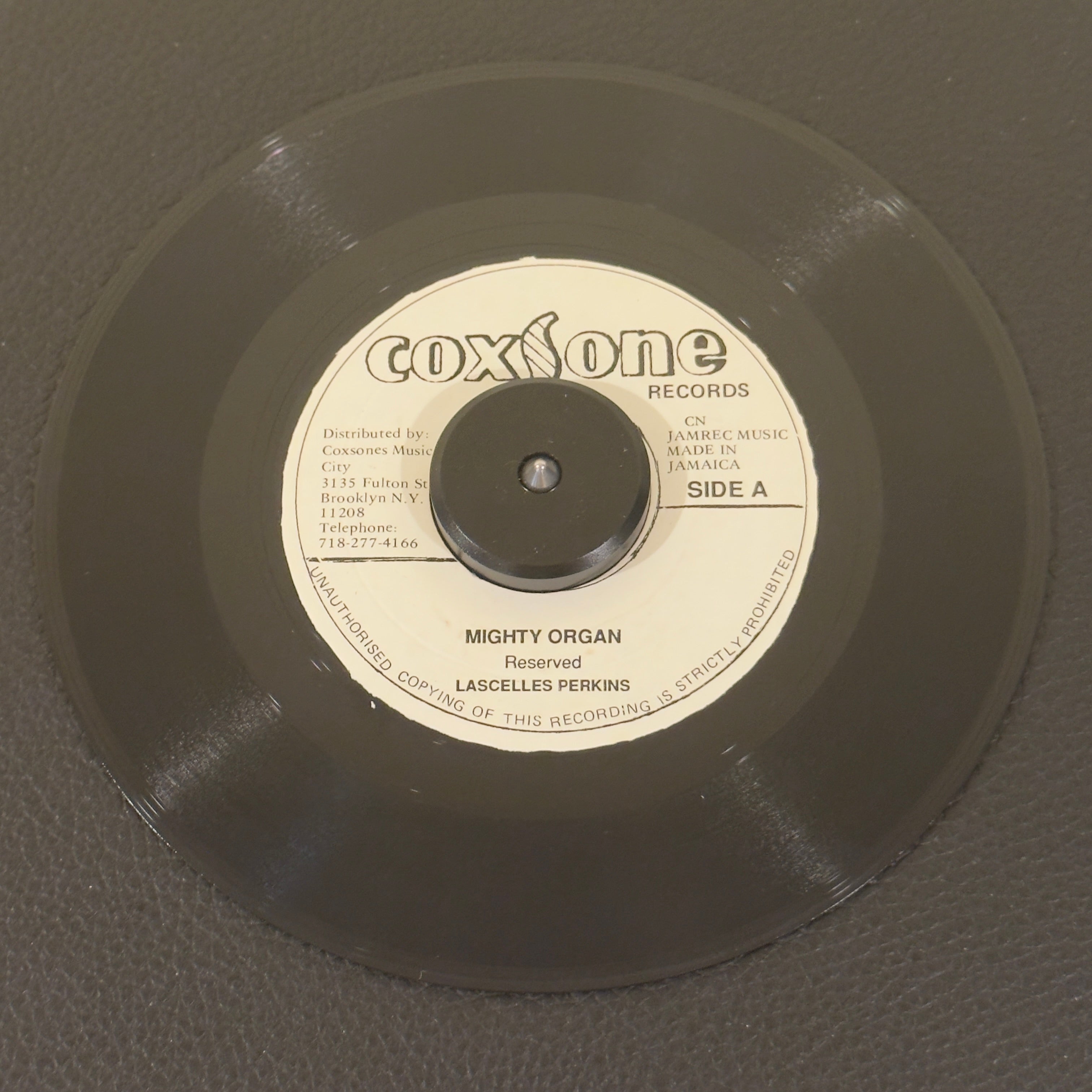 7" vinyl record by Lascelles Perkins featuring "Mighty Organ/Westbound No. 9 (Flaming Ember)", released on Coxsone Records (), in VG (Very Good) condition, classic analog collectable for turntable playback. Incredible piece of Jamaican vinyl manufacturing history: a rare, highly sought-after Coxsone Records hybrid split single! Westbound No 9 by The Flaming Embers on the B side.