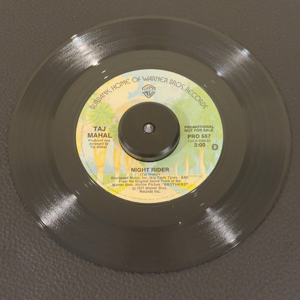 7" vinyl record by Taj Mahal featuring "Night Rider/Love Theme in the key of D", released on Warner Bros. Records (PRO 667), in VG+ (Very Good Plus) condition, classic analog collectable for turntable playback. An essential crossover piece for deep funk DJs, cinematic soundtrack collectors, and Taj Mahal completists.  Original WB sleeve included.