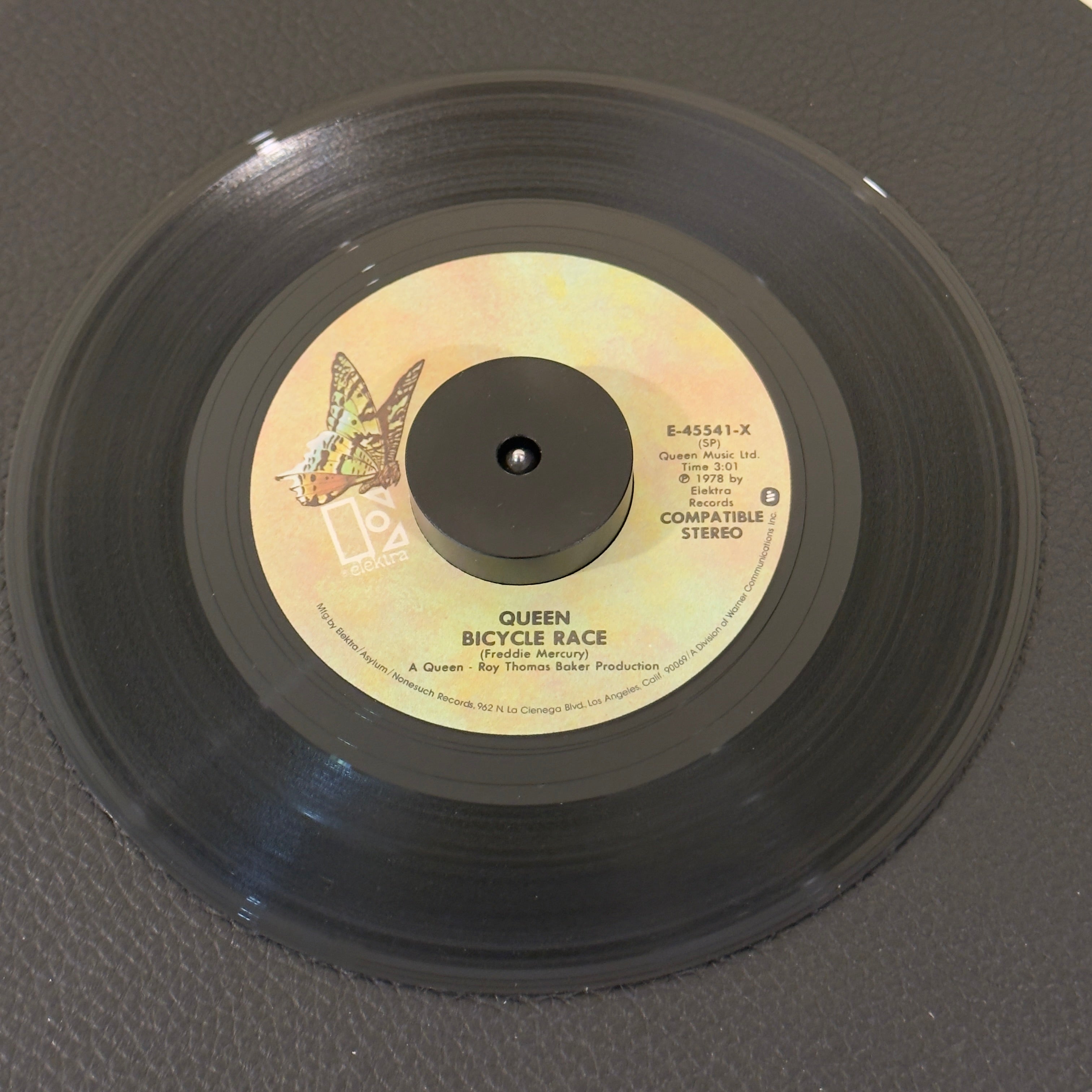 7" vinyl record by Queen featuring "Bicycle Race/Fat Bottom Girls", released on Elektra (E-45541), in VG+ (Very Good Plus) condition, classic analog collectable for turntable playback. Pic Sleeve included (Slight ring on front cover & left side of sleeve is open).  Butterfy label version.